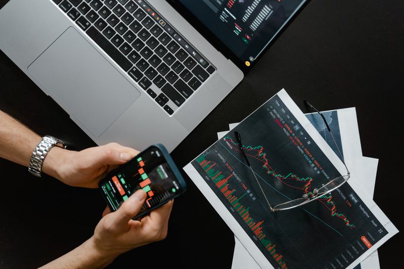 Primer plano de una mano sobre un teclado junto a una pantalla con gráficos financieros